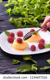 The Girl Is Going To Eat Delicious Panna Cotta With Caramel Sauce Small Teaspoon. A Woman Wants To Lose Weight And Eats A Dietary Dessert. Delicious Italian Pudding With Fresh Mint And Raspberries.