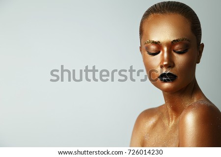 Girl with golden paint on her face. Black lipstick on lips. Creative make up, face art, body art