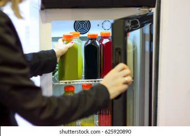 Girl grabbing cold pressed juice from refrigerator, green, red, black fruit drink in plastic bottles