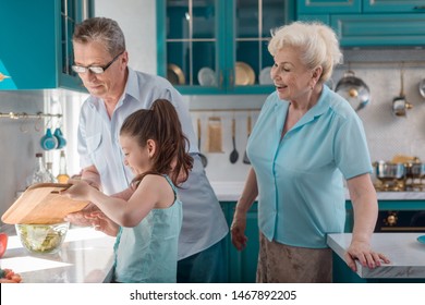 Girl and grandparents blending salad ingredients in kitchen. Generations of family. Teaching kids to cook.