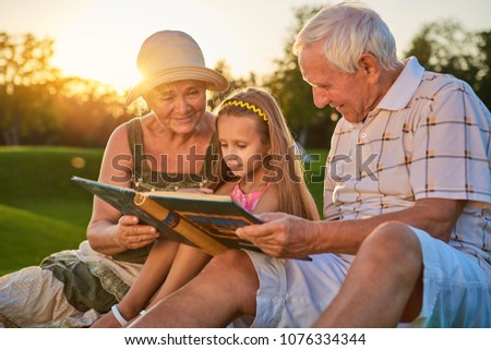 Girl with grandparents, photo album. People looking at photos outdoors. Many years ago.