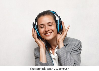 A Girl In A Gray Jacket And A White Shirt Listens To Music On Headphones During A Break From Business Affairs With A Smile