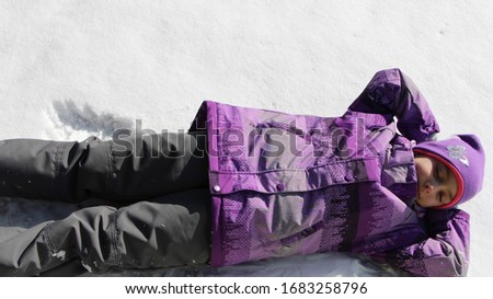 girl in a gray-lilac suit lies on the snow in a relax pose sunny day
