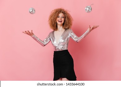 Girl In Great Mood Juggles With Mini Disco Balls. Portrait Of Curly Lady In Shiny Blouse On Pink Background