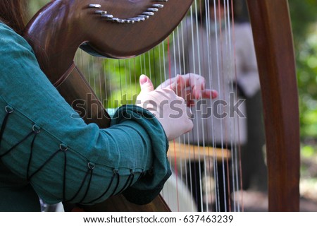 Girl in green dress plays on a Celtic harp in the summer garden