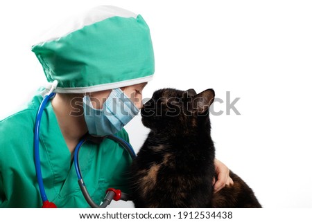 Girl in green medical surgical suit and protective medical mask plays veterinarian with domestic black cat Isolated on white. Look at each other