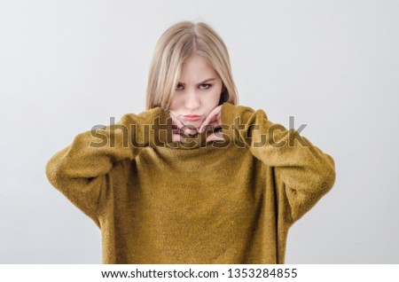Girl in a green sweater posing on white background. Offended, pensive.