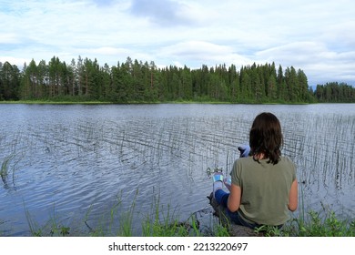 Girl In Green T-shirt Sitting At A Calm Lake. Swedish Summer Nature. Jämtland, Sweden, Europe.