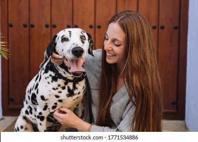 girl in grey dress with red hair smiling and hugging her Dalmatian dog