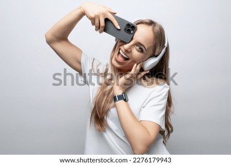 girl grimaces in wireless headphones with a smartphone in her hands on a white background
