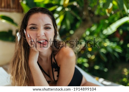 girl grimacs pressing her palm to her cheek with long nails behind her green palm trees. High quality photo