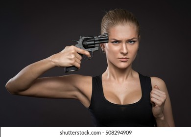 Girl With A Gun Holding The Revolver To Her Head Pretending To Shoot Herself Or Commit Suicide, Dark Background. 