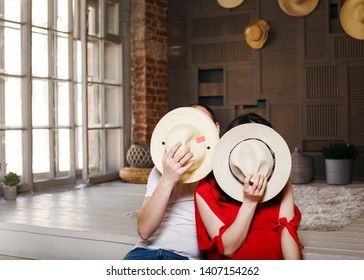 
The Girl And The Guy Cover Their Faces With A Hat. Husband And Wife Hid Behind Their Hats, Waiting For A Surprise. Two People Hid, No Face