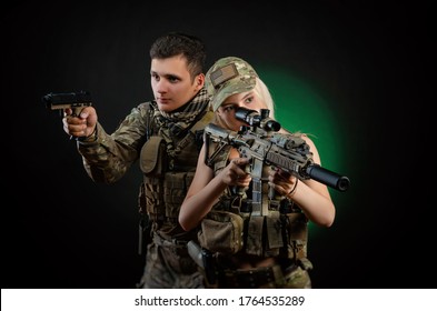 a girl and a guy in military overalls pose with an airsoft gun on a dark background