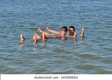 The Girl And The Guy Swims In The Dead Sea And Smile. Rest On The Sea. Family Vacation At Sea. Bathing In Salt Water.