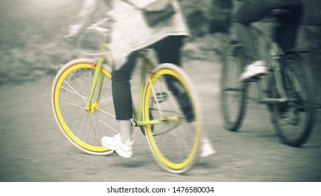 A girl and a guy together quickly ride on sports bikes in the Park on a summer day. The image is in a monochrome filter, and the girl's bike is yellow-green bright color.
