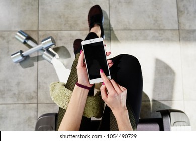 A Girl In A Gym Sitting Watching A Workout Schedule In The Phone. Top View