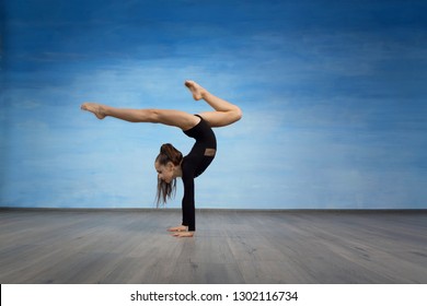 Girl gymnast in a black gymnastic swimsuit makes handstand on a blue sky background.
