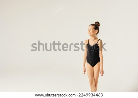 A girl gymnast in a black leotard smiles and looks away.