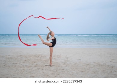 girl gymnast makes elements with a ribbon from rhythmic gymnastics, on the beach with a beautiful ribbon - Powered by Shutterstock