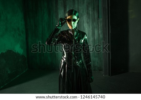 Girl hacker in the digital world. Young woman in matrix style suit. Black leather and sunglasses on black background