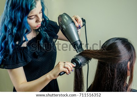 girl hairdresser with blue hair dries hair to the client in the beauty salon
