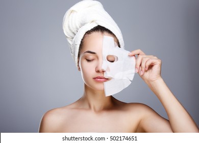 Girl with half rended white mask. Model pulling away mask from her face. Closed eyes. Head and shoulders, studio, indoors