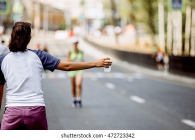 Girl In Hand A Cup Of At Water Point Of Marathon, In Background Runner