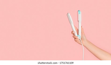 Girl Hand Holding Hair Straightener On Pink Background, Blank Space. Panorama