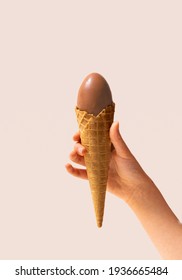 A Girl Hand Holding Ice Cream Cone With Chocolate Egg Arrangement. Bright Champagne Background.