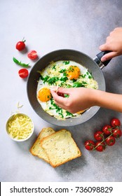 Girl Hands Above Frying Pan With Three Cooked Eggs, Herbs, Cheese, Tomatoes. Woman Is Making Breakfast. Top View. Copy Space