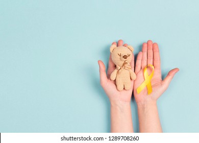 Girl hands holding children's toy with a Childhood Cancer Awareness Yellow Ribbon on blue background. Childhood Cancer Day February, 15. - Powered by Shutterstock