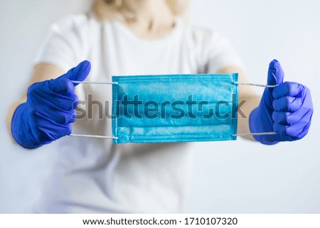 A girl with hands in medical gloves holds a protective mask 	