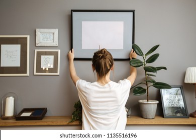 Girl hanging a frame on a gray wall, sun light - Shutterstock ID 1135516196