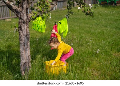 Girl hangs wet laundered clothes on a clothesline under a tree in garden. Washing detergents for colored laundry. Preservation of the brightness of the juiciness of the color of fabrics when washing
