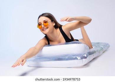 A girl with a happy smile lying on an inflatable mattress imitates floatation in a swimsuit on a blue neon background. Summer rest.
