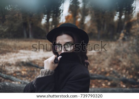 A girl has a programmatic code reflected in her glasses. She covers her face with the coat's collar and stands on a forest background.
