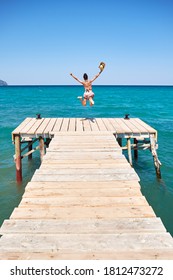 Girl With Hat Jumping On A Wooden Wharf