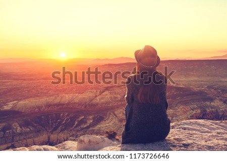 A girl in a hat on top of a hill in silence and loneliness admires a tranquil natural landscape in search of a soul.