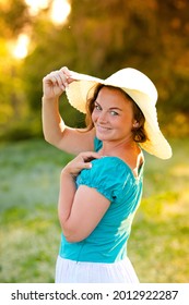 a girl in a hat stands with her back and turns to the camera in a chamomile field during sunset