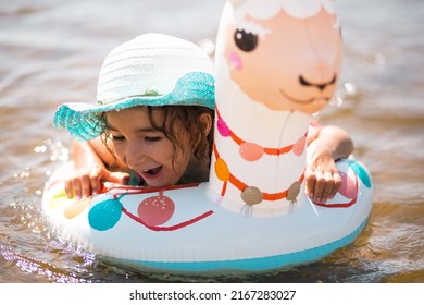 Girl in a hat it stands on the shore with inflatable circle in the shape of a lama. Inflatable alpaca for a child. Sea with a sandy bottom. Beach holidays, swimming, tanning, sunscreens.