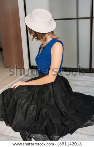 a girl in a hat and a tutu skirt is sitting on the floor in an apartment