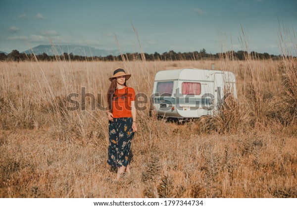 Girl with hat walking on the field during\
summer day with camp house behind her.\
