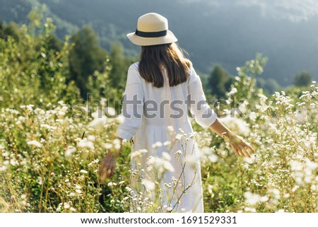 A girl in a hat and a white dress walks in a clearing in summer