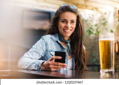 Girl having a beer while waiting for a friend. Long haired woman drinking beer at a bar. Girl in a flannel shirt at a bar. - Powered by Shutterstock