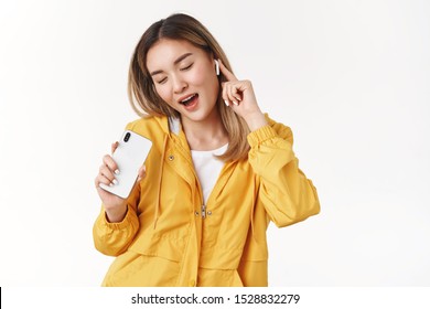 Girl having fun enjoy listen music close eyes cheerful carefree relaxing hear awesome track use mobile song platform app singing along in smartphone touch wireless white earbud, studio background