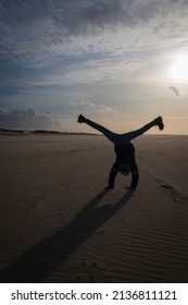 A girl having fun on a beach doing a cartwheel against the sun