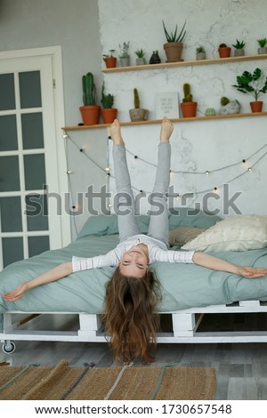 girl having fun in sofa.Teenage girl is fooling around on bed, hanging upside down,legs up.Portrait of charming teen rejoice lie bed big light bedroom.Lifestyle concept.Quarantine at home.Vacation
