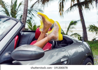 Girl having fun in tropical country laying in stylish luxury car in crazy bright clear boots.