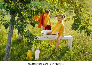 A girl is having fun washing clothes in the fresh air under a tree at sunset. Sister hangs wet clean clothes to dry on a clothesline